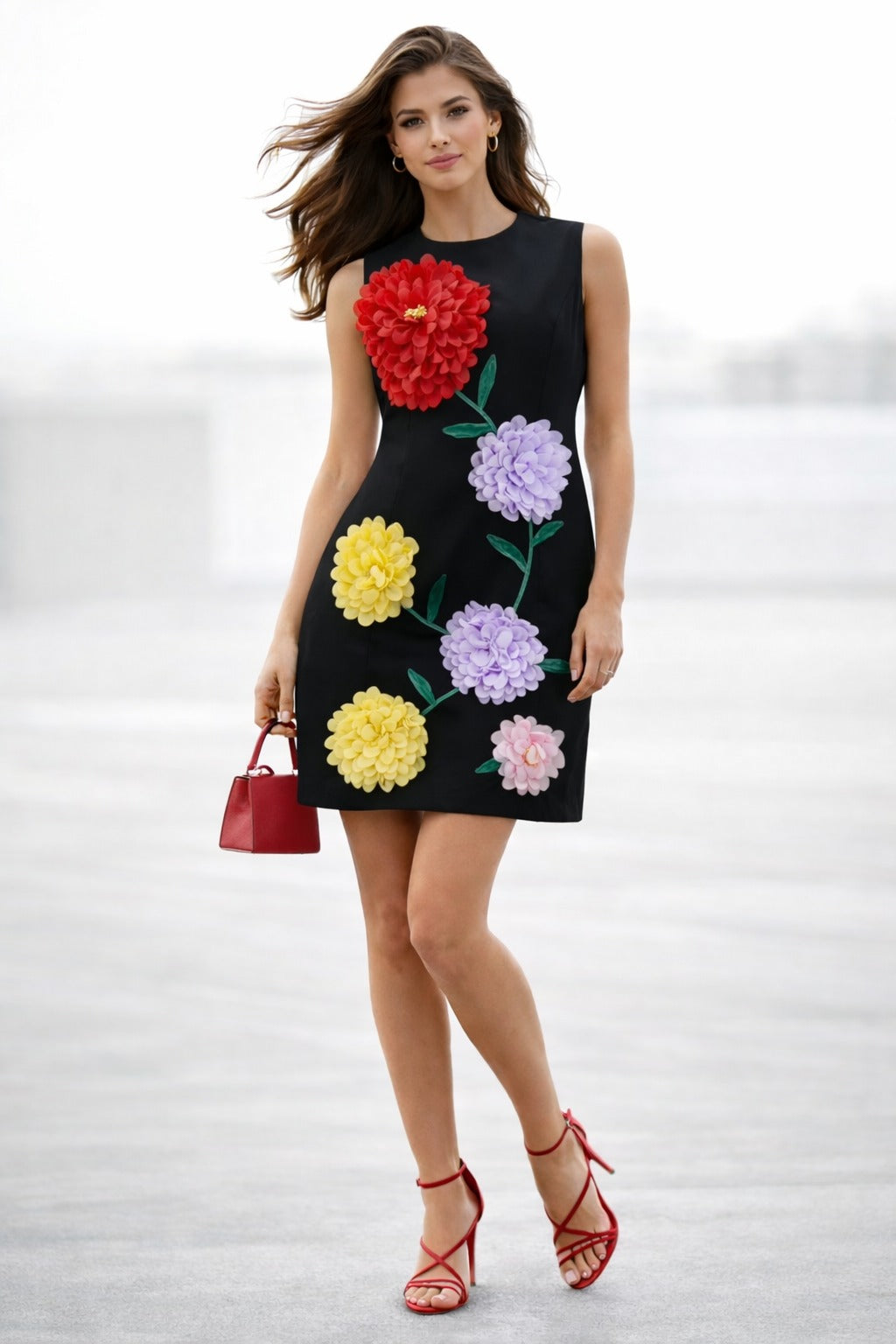 Woman wearing a black sleeveless mini dress decorated with oversized red, lavender, yellow, and blush floral appliqués
